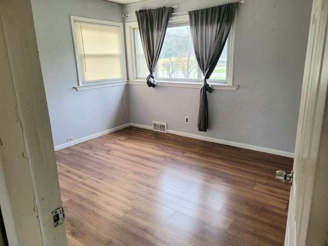 unfurnished room featuring visible vents, baseboards, and wood finished floors