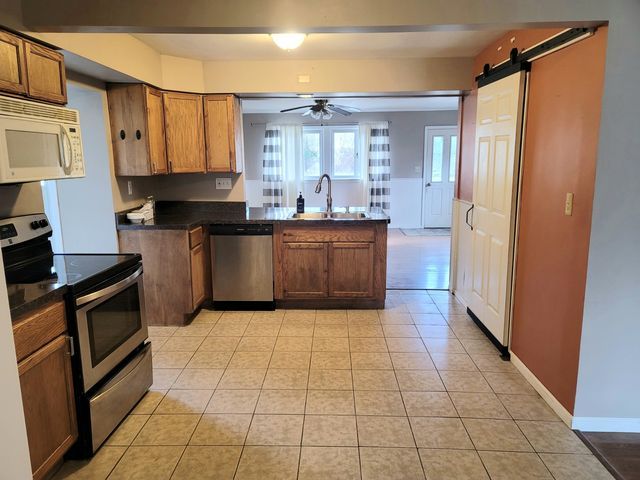 kitchen featuring a sink, dark countertops, stainless steel appliances, a peninsula, and light tile patterned floors