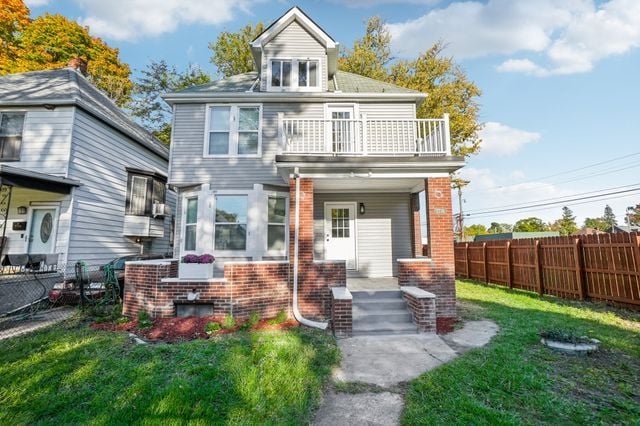 3736 Iroquois St, Detroit, MI 48214 - view of front facade with brick siding, a front lawn, fence, covered porch, and a balcony