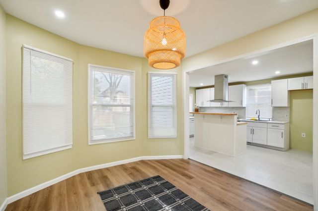 3736 Iroquois St, Detroit, MI 48214 - kitchen with baseboards, light wood-style flooring, island exhaust hood, a sink, and white cabinetry