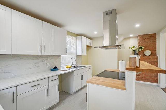 3736 Iroquois St, Detroit, MI 48214 - kitchen featuring tasteful backsplash, black electric stovetop, island range hood, white cabinets, and a sink