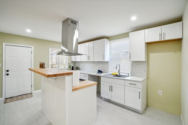 3736 Iroquois St, Detroit, MI 48214 - kitchen with a sink, decorative backsplash, butcher block countertops, white cabinets, and island range hood