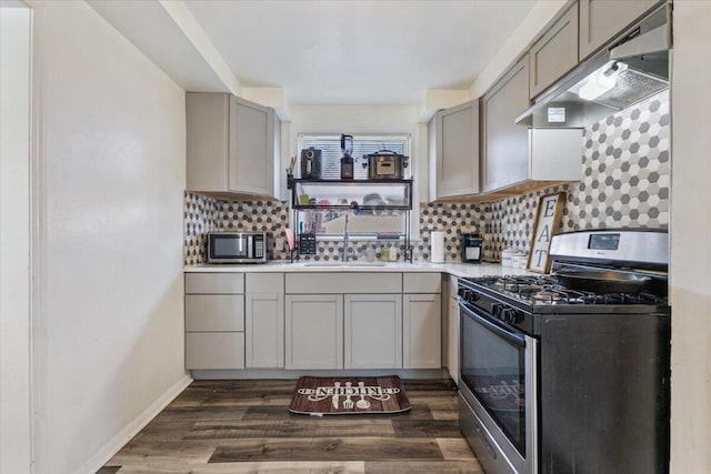 kitchen with a sink, gray cabinetry, appliances with stainless steel finishes, under cabinet range hood, and tasteful backsplash