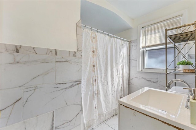 full bath with marble finish floor, tile walls, a shower with curtain, and a sink