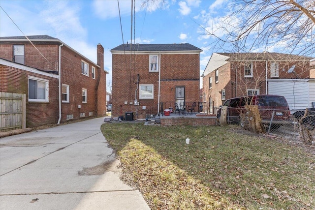 back of property featuring a yard, brick siding, central AC unit, and fence