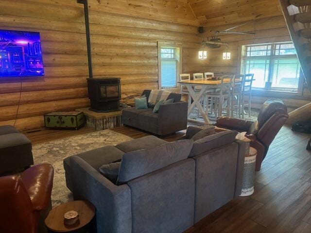 living area with log walls, wood finished floors, a wood stove, and vaulted ceiling