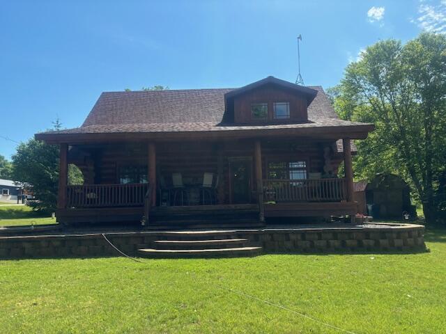 rear view of house featuring log exterior, covered porch, and a yard