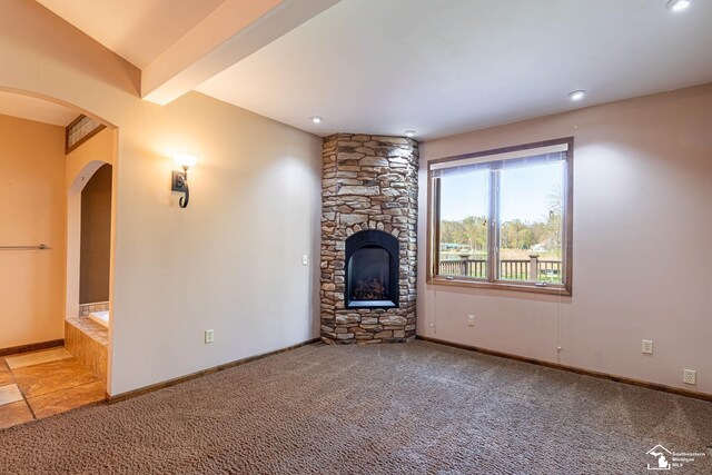 unfurnished living room with carpet floors, arched walkways, baseboards, and a fireplace