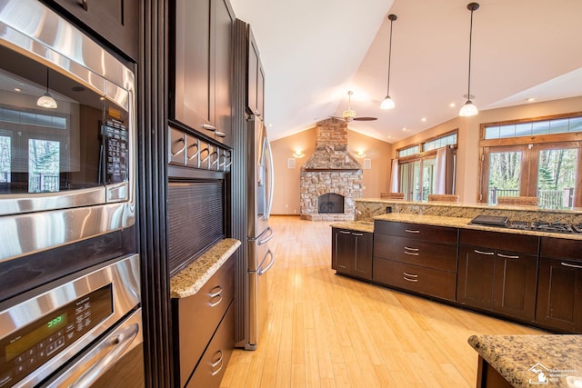 kitchen featuring ceiling fan, a fireplace, wall oven, dark brown cabinets, and light wood-style flooring