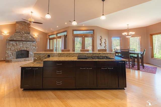 kitchen featuring pendant lighting, vaulted ceiling, gas stovetop, ceiling fan with notable chandelier, and light wood finished floors