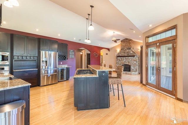 kitchen with a ceiling fan, arched walkways, light wood-type flooring, beverage cooler, and stainless steel appliances