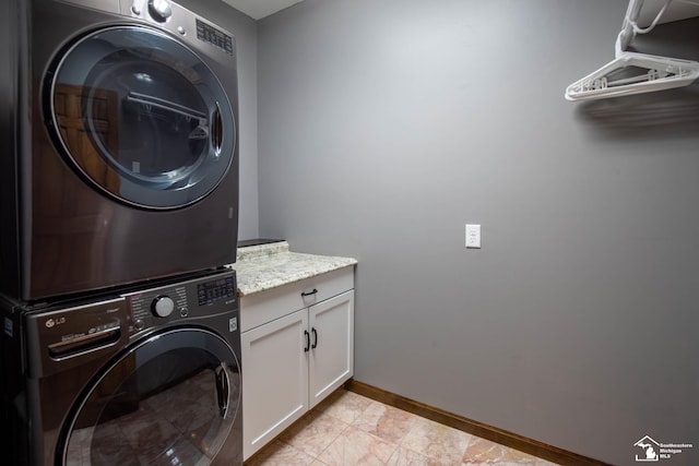 washroom featuring baseboards, stacked washer and dryer, and cabinet space