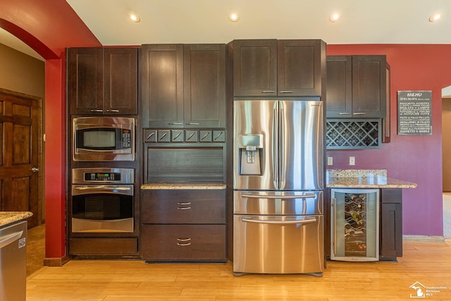 kitchen featuring beverage cooler, light wood-type flooring, light stone counters, arched walkways, and appliances with stainless steel finishes