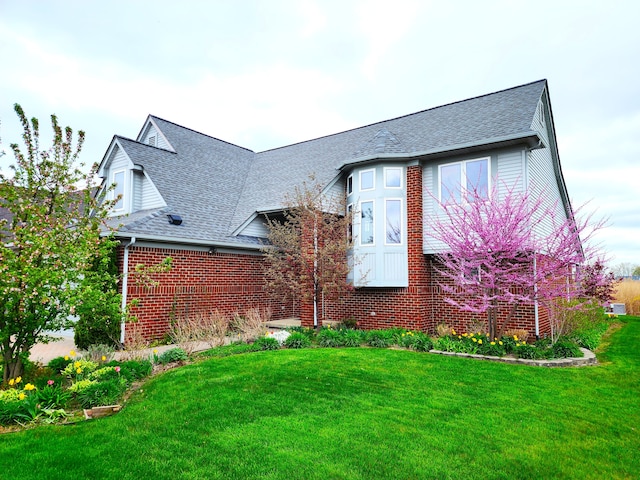 view of front facade with a front lawn, brick siding, and roof with shingles
