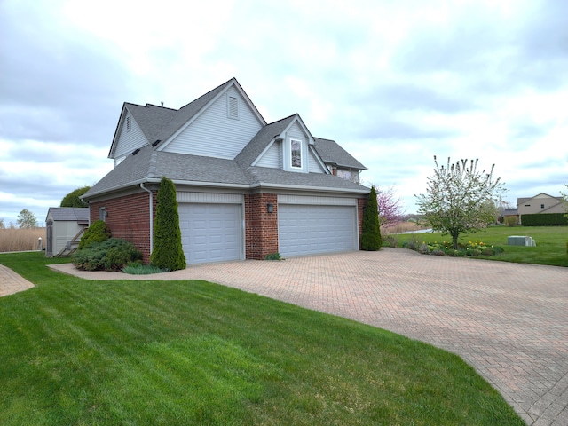 view of side of property featuring an attached garage, brick siding, a yard, decorative driveway, and a shingled roof