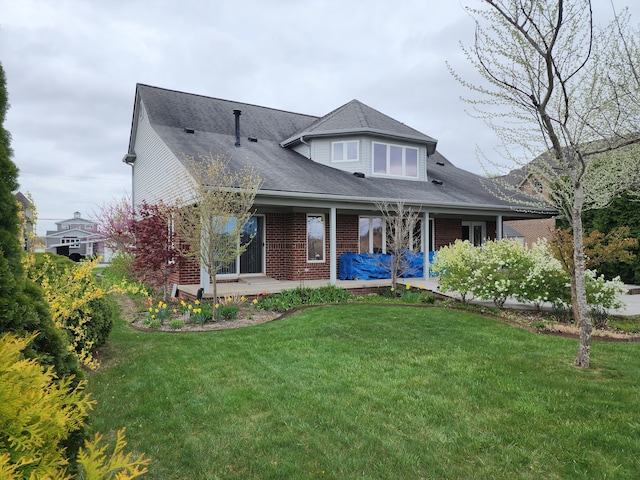 view of front of home with a front yard, roof with shingles, and brick siding