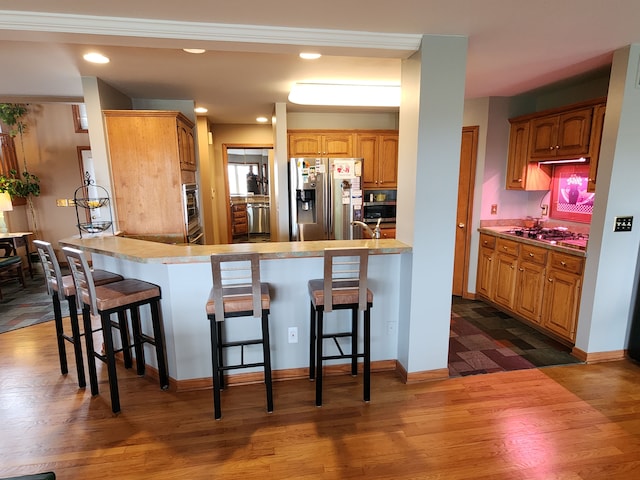 kitchen featuring a peninsula, appliances with stainless steel finishes, dark wood-type flooring, and a kitchen breakfast bar