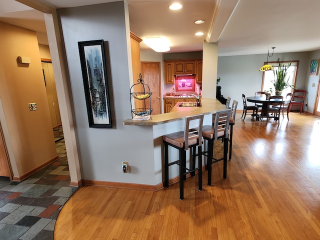 kitchen featuring wood finished floors, brown cabinets, a sink, a kitchen breakfast bar, and baseboards