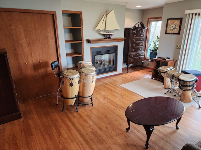 living room with a glass covered fireplace, built in features, and wood finished floors