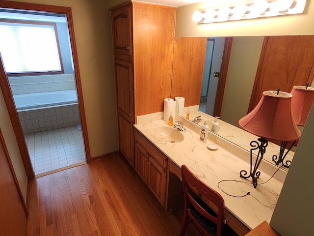 full bathroom featuring baseboards, tiled tub, vanity, and wood finished floors