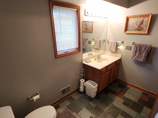 bathroom featuring toilet, baseboards, stone finish flooring, and visible vents