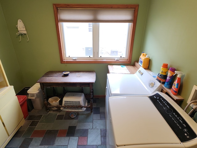 clothes washing area featuring stone tile flooring, washing machine and dryer, plenty of natural light, and laundry area