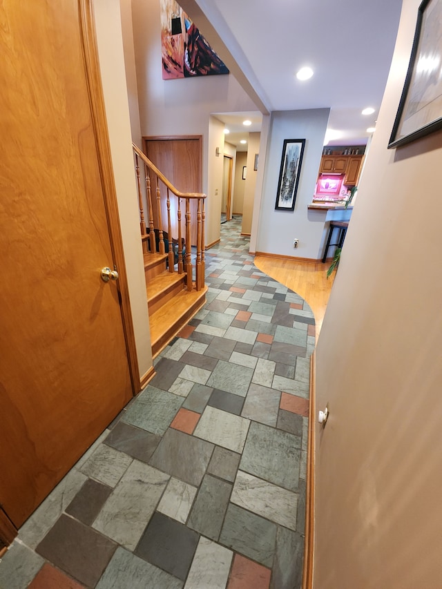 corridor with stone tile flooring, stairway, baseboards, and recessed lighting
