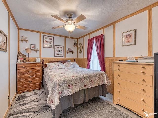 bedroom featuring a wainscoted wall, light colored carpet, a textured ceiling, and ornamental molding