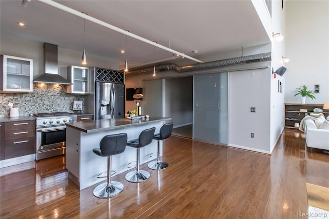 100 N Center St Unit 302, Royal Oak, MI 48067 - kitchen featuring stainless steel appliances, wall chimney exhaust hood, a kitchen breakfast bar, glass insert cabinets, and dark wood-style flooring