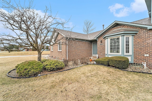 view of side of home featuring a yard, brick siding, and roof with shingles