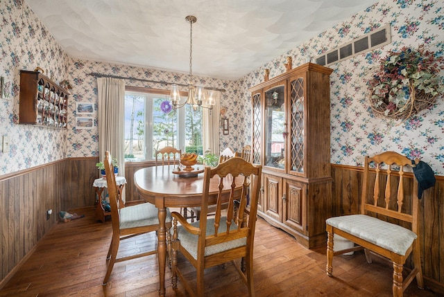 dining room featuring a notable chandelier, a wainscoted wall, wallpapered walls, and light wood-style floors