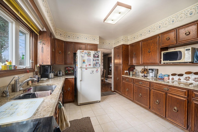 kitchen with wallpapered walls, white appliances, light stone counters, and a sink