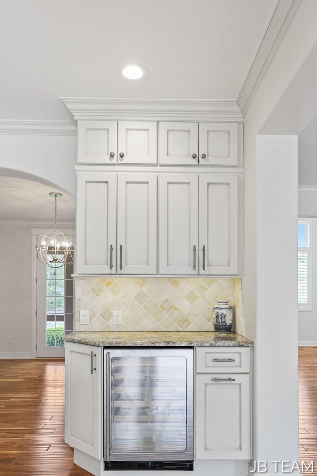 6579 Partridge Ln, Holland, MI 49423 - indoor dry bar featuring wine cooler, ornamental molding, arched walkways, wood finished floors, and baseboards