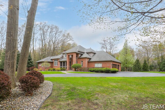 6579 Partridge Ln, Holland, MI 49423 - view of front of house with brick siding, curved driveway, a garage, a front yard, and a shingled roof