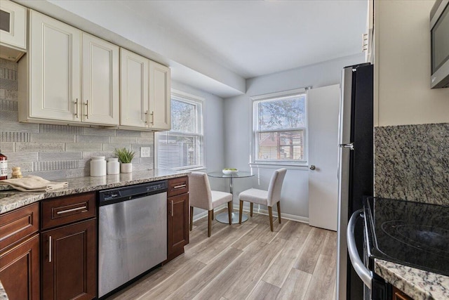 kitchen featuring light wood finished floors, tasteful backsplash, light stone counters, white cabinets, and stainless steel appliances