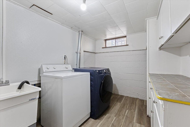 laundry room with concrete block wall, light wood-type flooring, cabinet space, a sink, and independent washer and dryer
