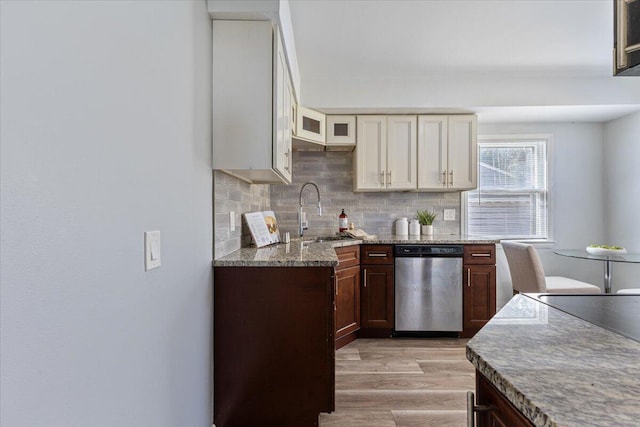 kitchen with light stone counters, a sink, light wood-style floors, stainless steel dishwasher, and tasteful backsplash