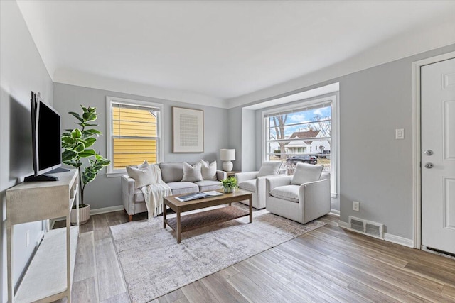 living room with wood finished floors, visible vents, and baseboards