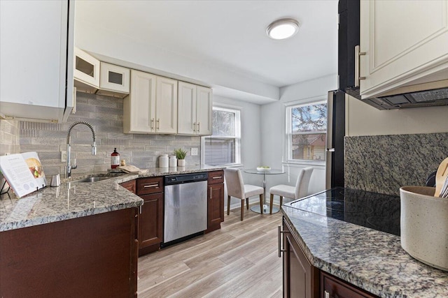 kitchen featuring light wood finished floors, dishwasher, light stone counters, decorative backsplash, and a sink