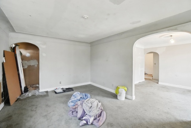 carpeted empty room featuring arched walkways and baseboards