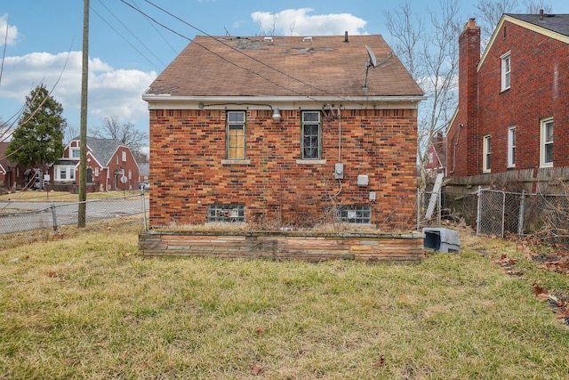 rear view of house with brick siding, a fenced backyard, a shingled roof, and a yard