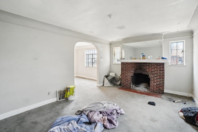 living room featuring a brick fireplace, plenty of natural light, arched walkways, and carpet floors