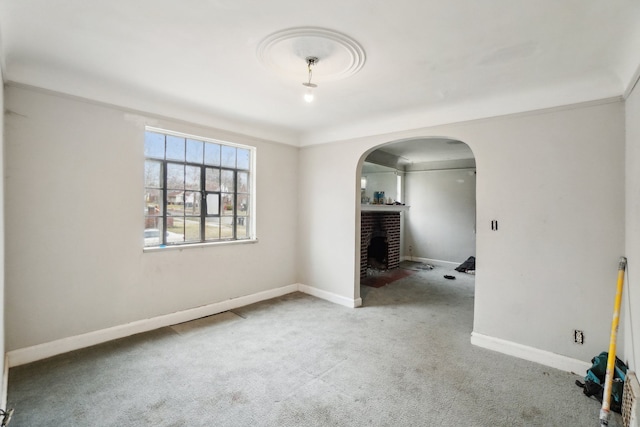 carpeted empty room with arched walkways, a fireplace, and baseboards