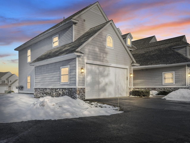 view of home's exterior featuring aphalt driveway, stone siding, a garage, and a shingled roof