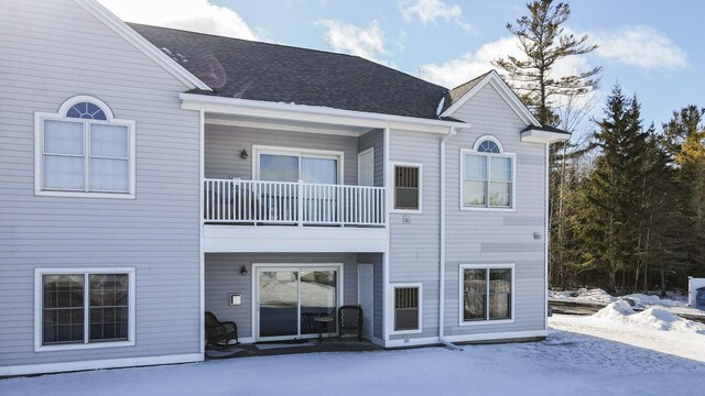 snow covered back of property with a balcony and a shingled roof