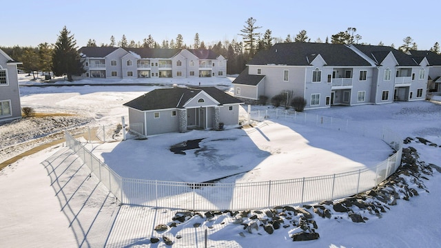 snow covered back of property featuring a fenced backyard, a residential view, and an outdoor structure