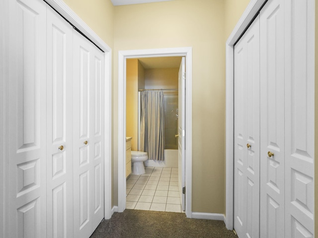 hallway featuring baseboards, light colored carpet, and light tile patterned flooring
