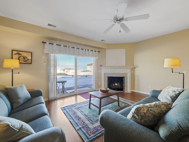 living room with visible vents, baseboards, ceiling fan, a fireplace, and wood finished floors