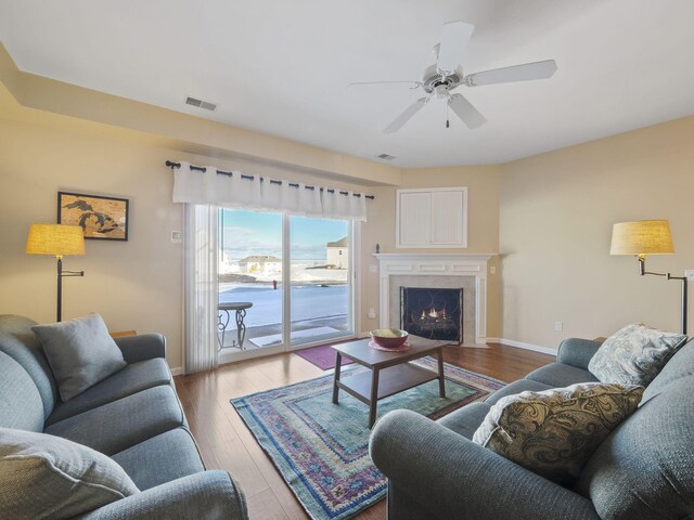 living area with a ceiling fan, baseboards, visible vents, a fireplace, and hardwood / wood-style flooring