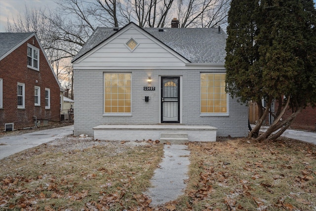 bungalow featuring brick siding, a chimney, and a shingled roof
